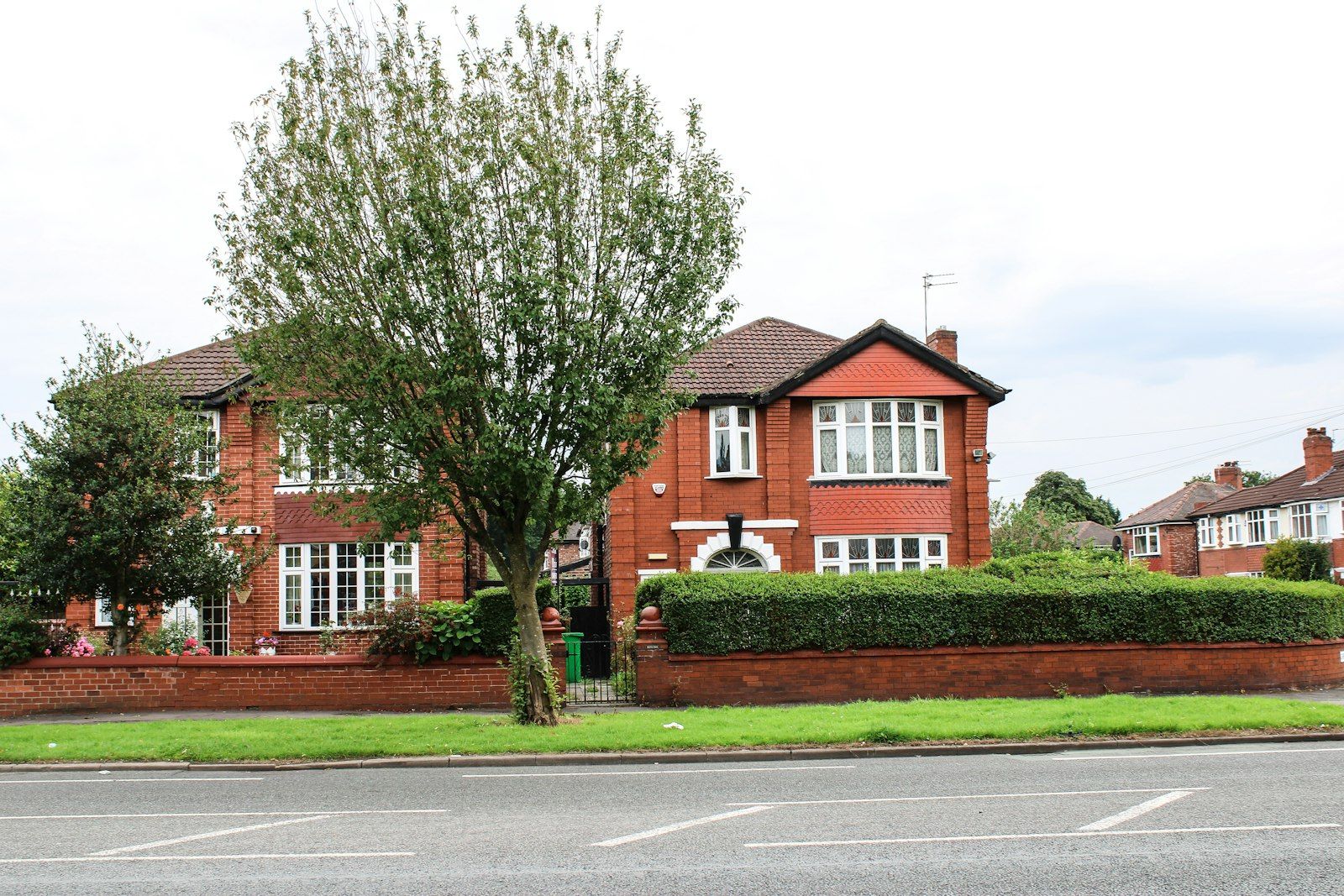 A red-brick 1930s semi-detached house behind a tree, typical of Warrington's suburbs